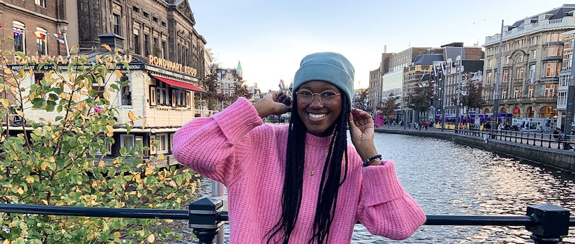 Student smiling and holding beanie on top of head in front of a river