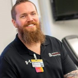 Male standing on top of a treadmill on campus smiling.