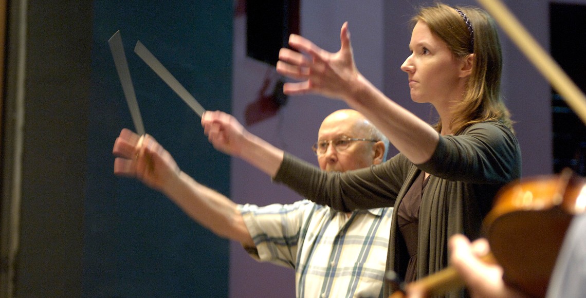 a professor and student wave batons to conduct a university orchestra