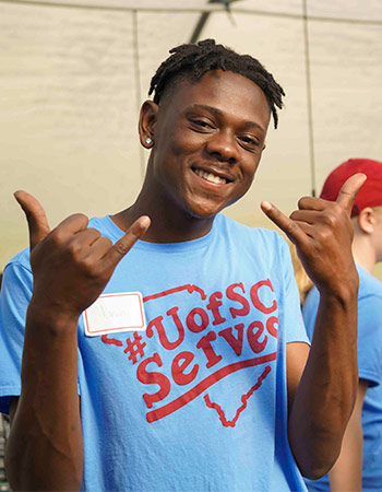 Student wearing a UofSC Serves t-shirt holding spurs up gesture and smiling at the camera. 