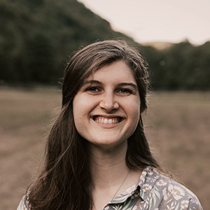 Photo of Sara smiling in a field with a flower dress on. 