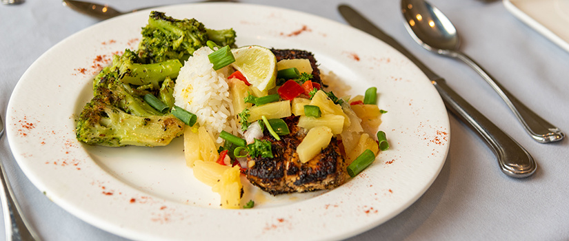 A plate of food with broccoli and pork covered with rice, pineapple, chives and topped with a lime.