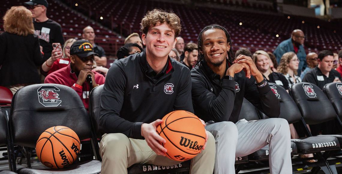 Two students on the bench at a basketball game at Colonial Life Arena.