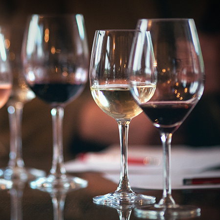 Two glasses of red and white wine are seen in the foreground with more blurred glasses behind them.