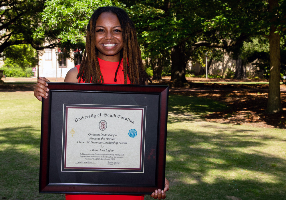 ethena inez lighty stands on the horseshoe holding a large framed award