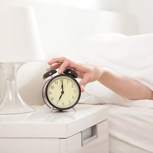 Detail shot of hand reaching from bed to nightstand to silence alarm clock.