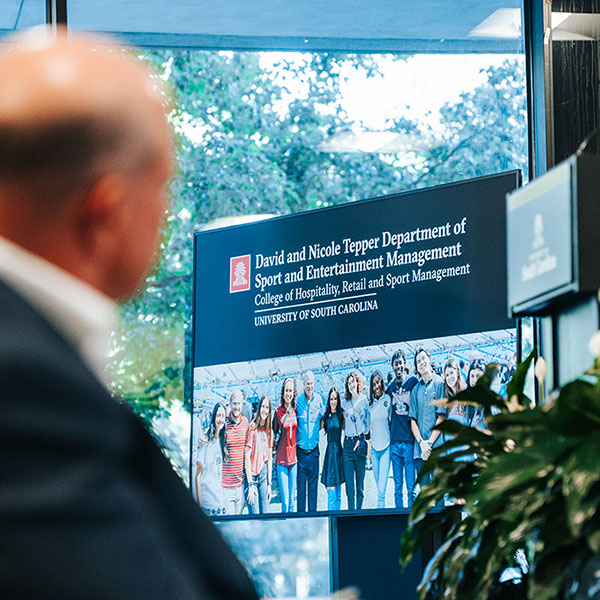 Carolina Panthers owner David Tepper looking toward video screen displaying logo and photo of students