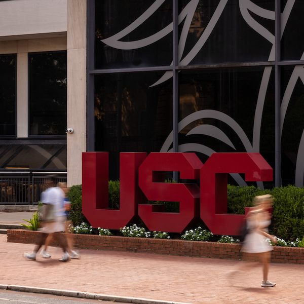 bold garnet USC letters outside of a gray building with students walking by