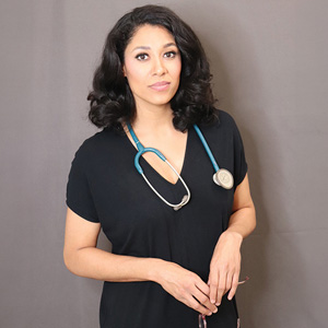 woman stands in hospital scrubs with stethoscope around her neck.