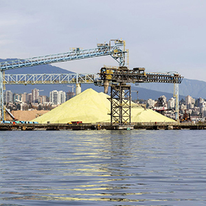 A pile of sulfur sits near a crane at a seaport